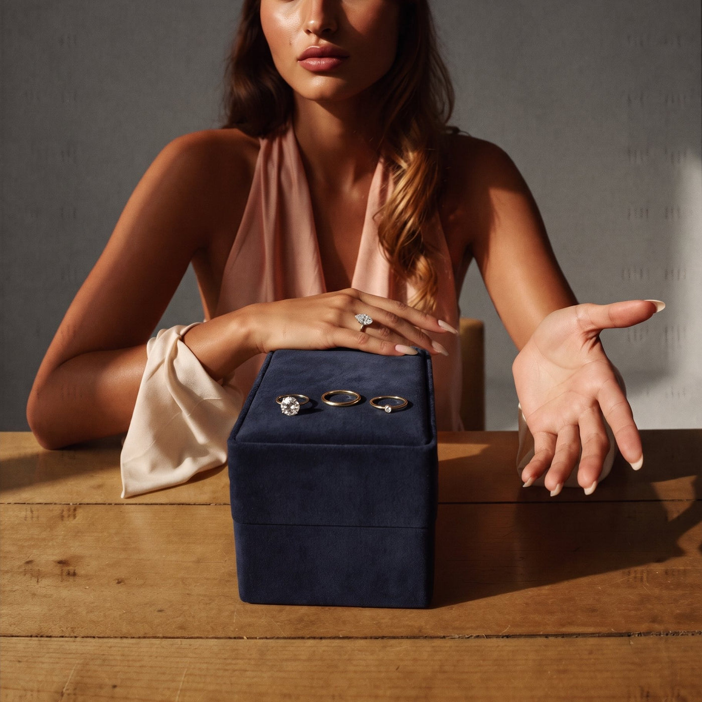Hands resting on a timber table beside a navy suede roll of gold diamond rings
