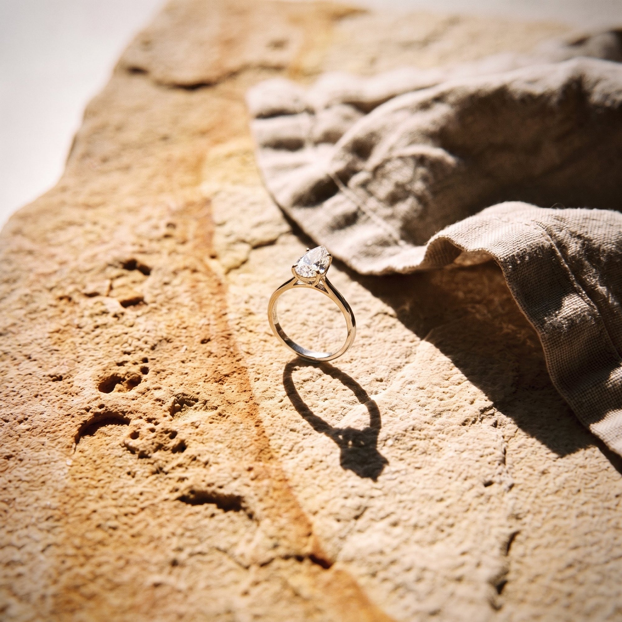 Gold pear diamond solitaire ring resting on sun-warmed sandstone