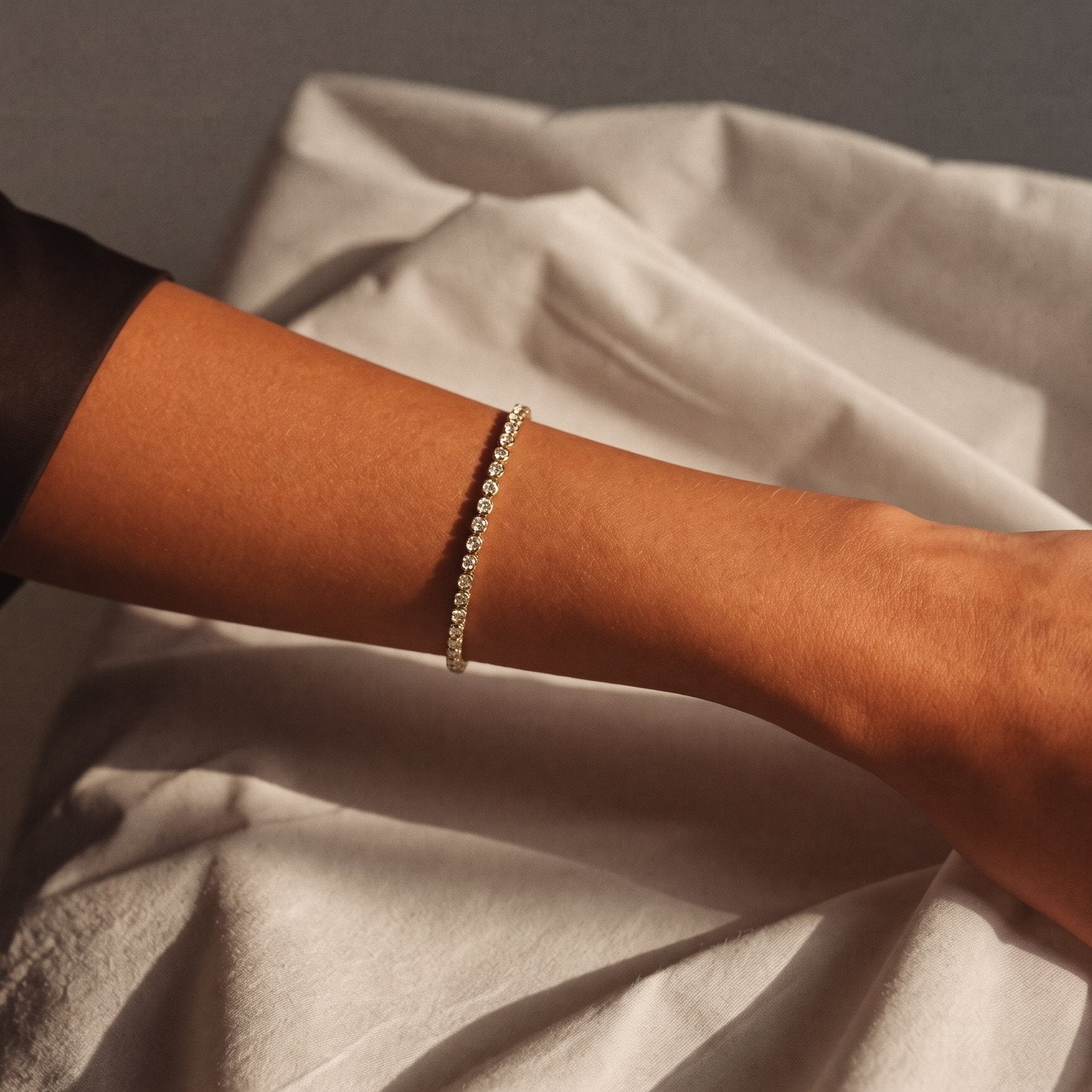Gold bezel-set diamond line bracelet on an inner wrist against white linen