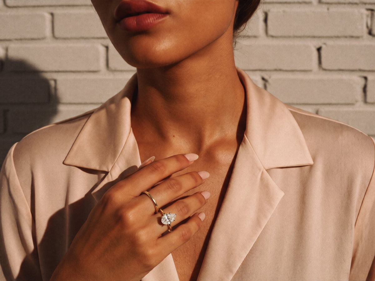 Hand held at the collarbone wearing a gold pear diamond solitaire ring and slim gold band