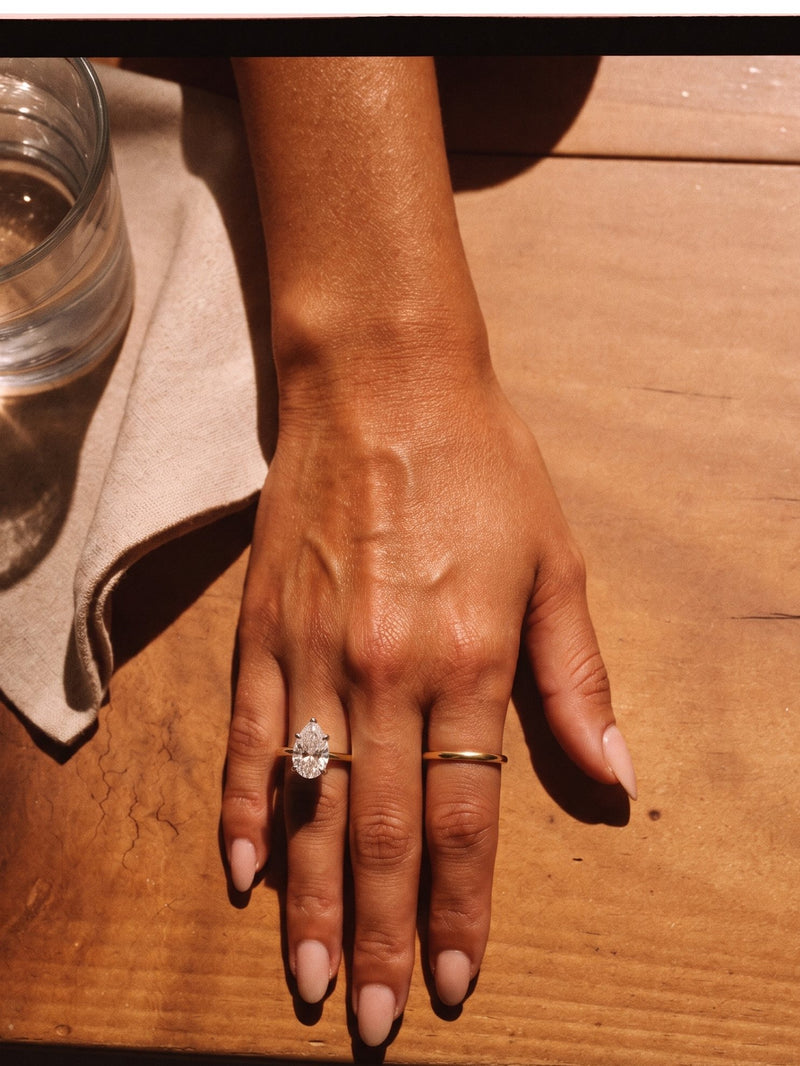 Overhead view of a hand on a timber table wearing a gold pear diamond solitaire and slim band