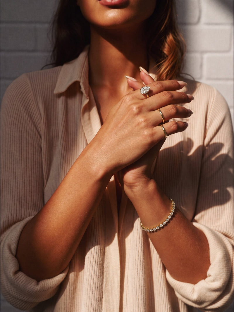Two cupped hands wearing a gold diamond line bracelet and pear solitaire ring in shutter light